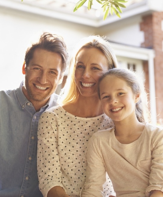 Family of three smiling outdoors on sunny day