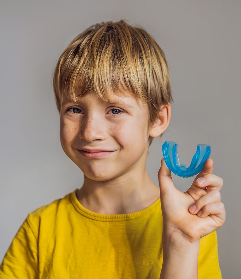 young child smiling and holding mouthguard