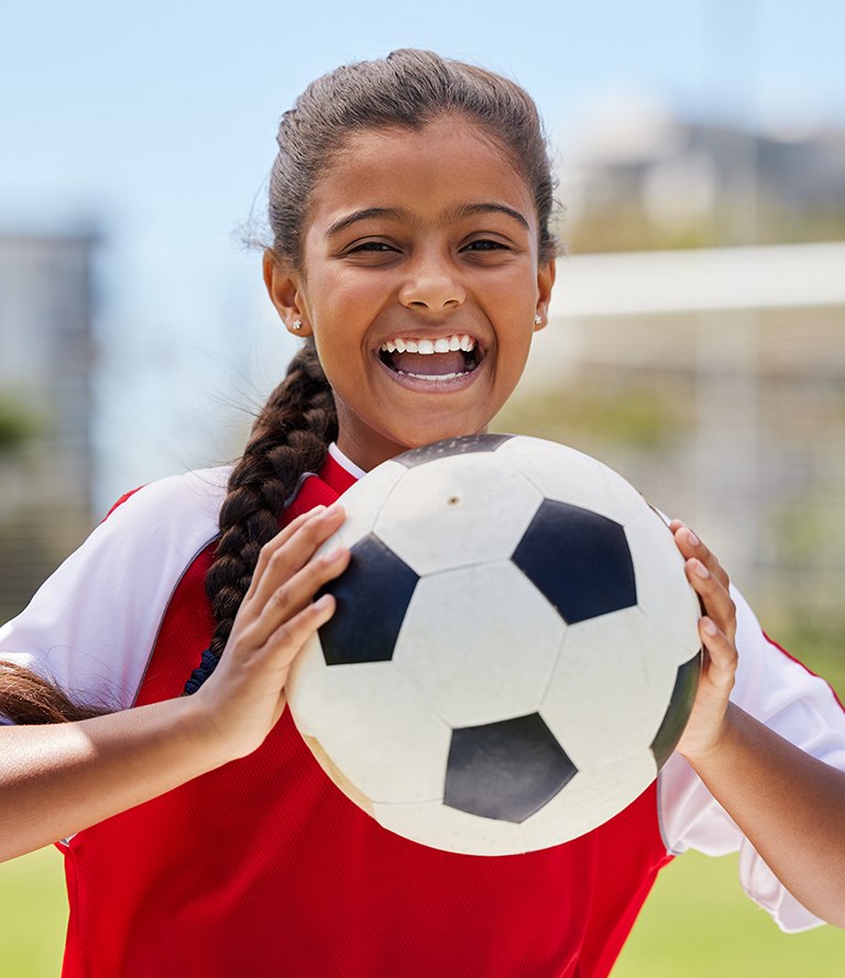 young child smiling while holding soccer ball 