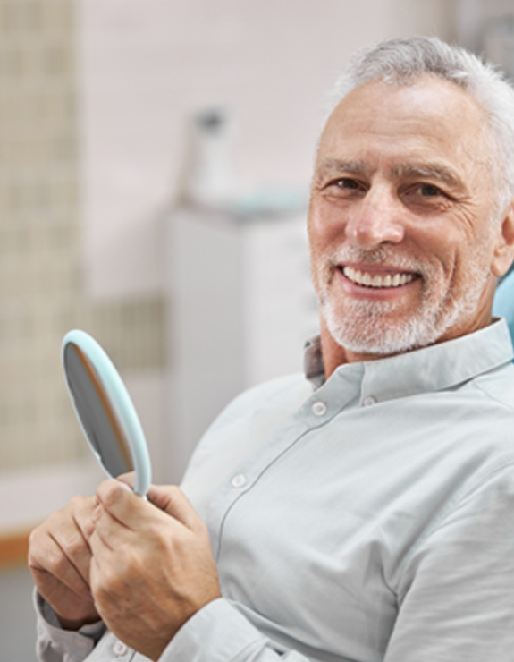 Senior man smiling in the dental chair while holding a mirror