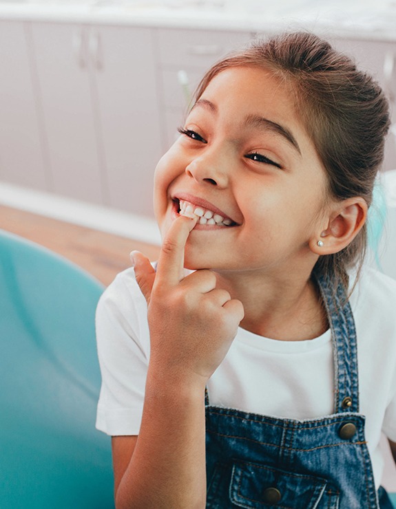 young child smiling and pointing to teeth 